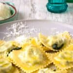 Spinach Ricotta ravioli on a off white plate with a sprinkle of finely grated cheese.