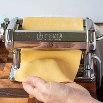 Pasta dough being rolled through the rollers of a hand cranked pasta machine.