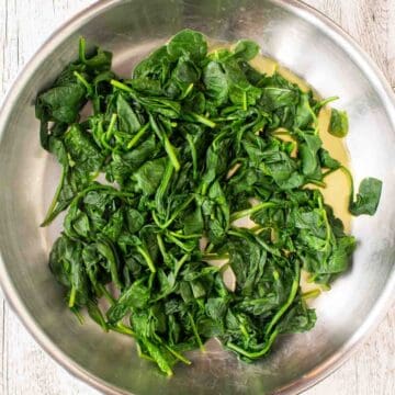 Overhead view of spinach being cooked in a stainless steel pan.