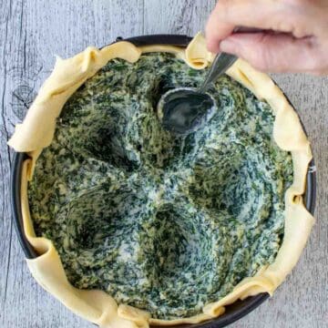 Overhead view of pie filled with spinach filling with five indentations in the filling.
