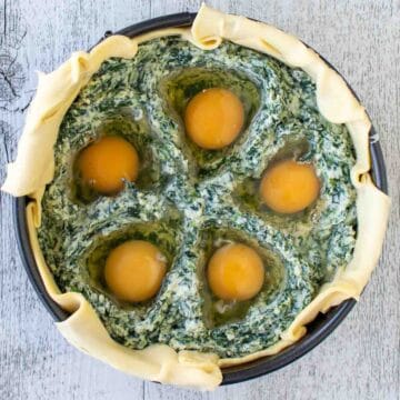 Uncooked spinach pie with five raw eggs nestled into the filling viewed from above.