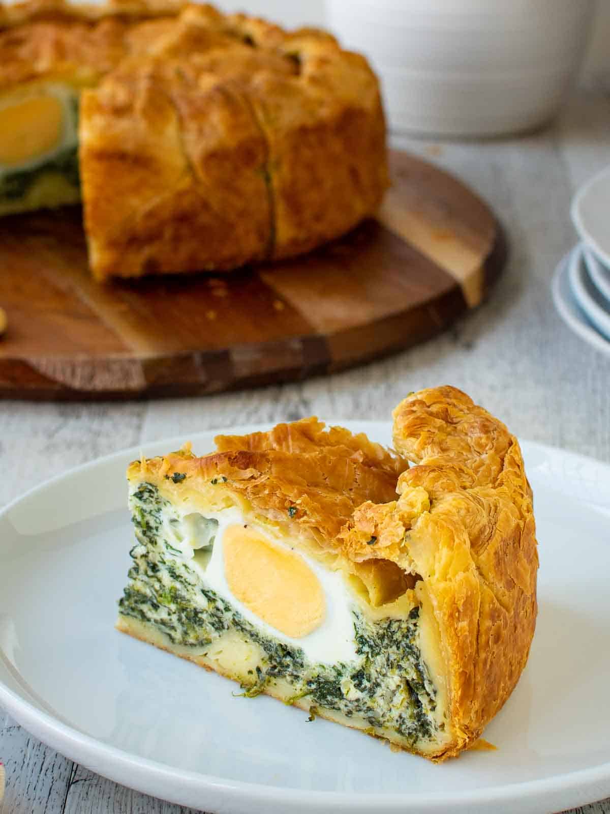 A slice of torta pasqualina on a white plate showing a hard boiled egg in spinach filling.