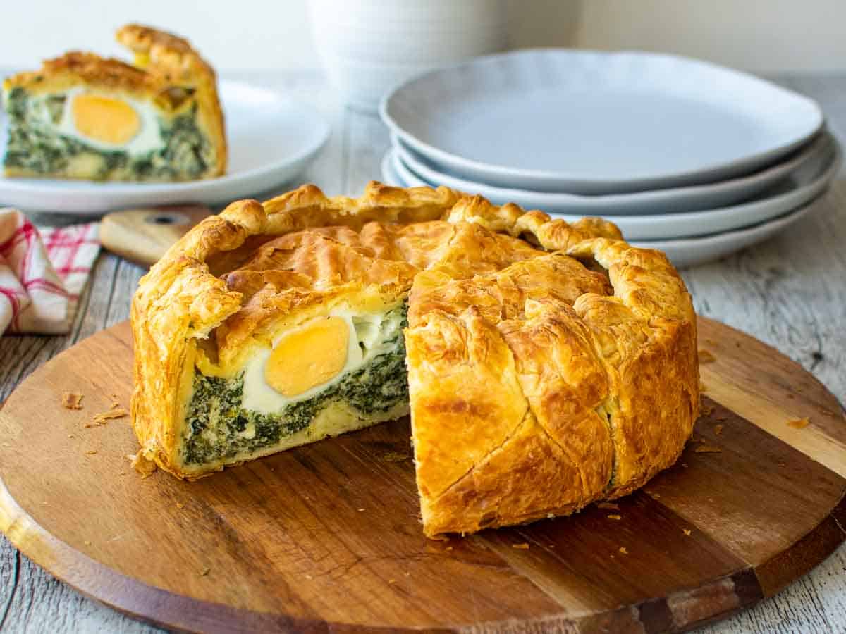 Pie with a slice cut out showing hard boiled eggs nestled in spinach filling.