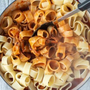 Calamari ring shaped pasta being stirred into tomato sauce.