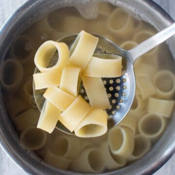 Cooked calamari-like pasta in a slotted spoon suspended above pasta pot.