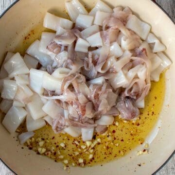 Chopped calamari added to pan of garlic, red pepper flakes and oil viewed from above.