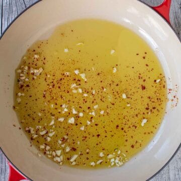 Garlic, red pepper flakes and olive oil in a pan viewed from above.