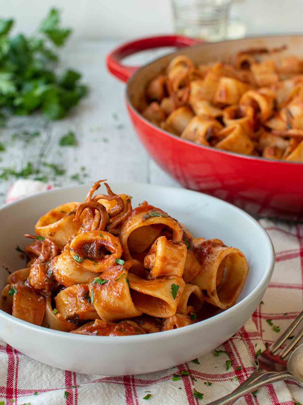 Calamarata pasta in a bowl on red check cloth with red pan in the background.