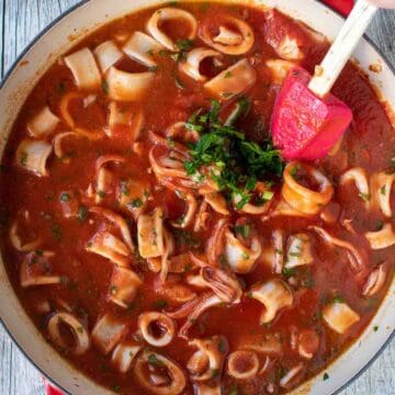 Calamari rings in tomato sauce and a handful of chopped parsley in a pan viewed from above.