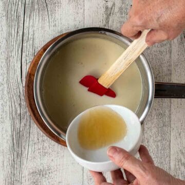 Yellowish liquid being added to saucepan filled with cream and coconut milk.