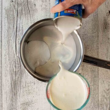 Cream and coconut milk being poured into a saucepan simultaneously.