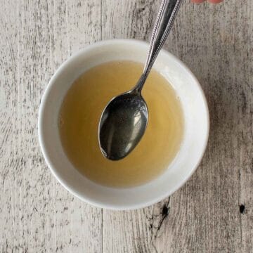 Yellowish liquid in a white bowl with a spoonful being lifted out.