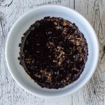 Dark brown liquid with coffee granules floating in a white bowl.
