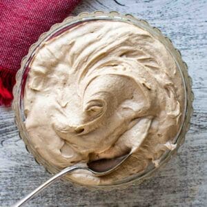 Coffee Buttercream in a glass bowl with spoon inserted viewed from above.