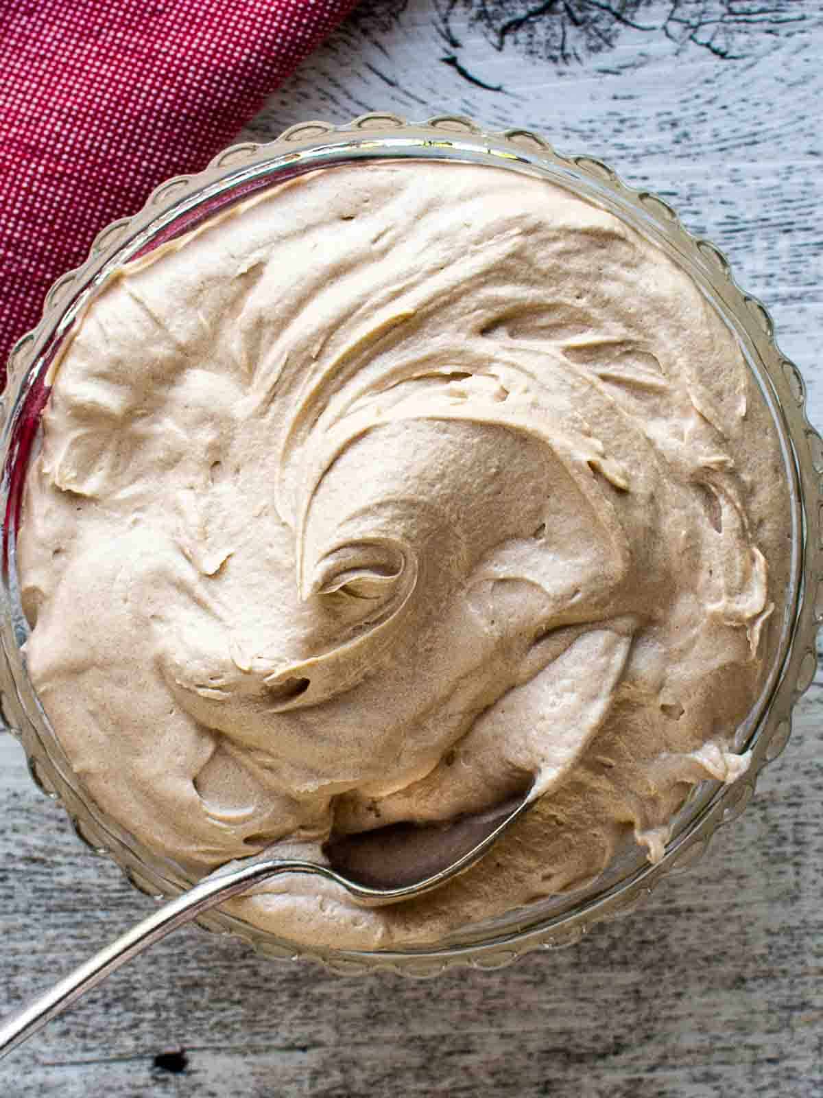 Coffee Buttercream in a glass bowl with spoon inserted viewed from above.