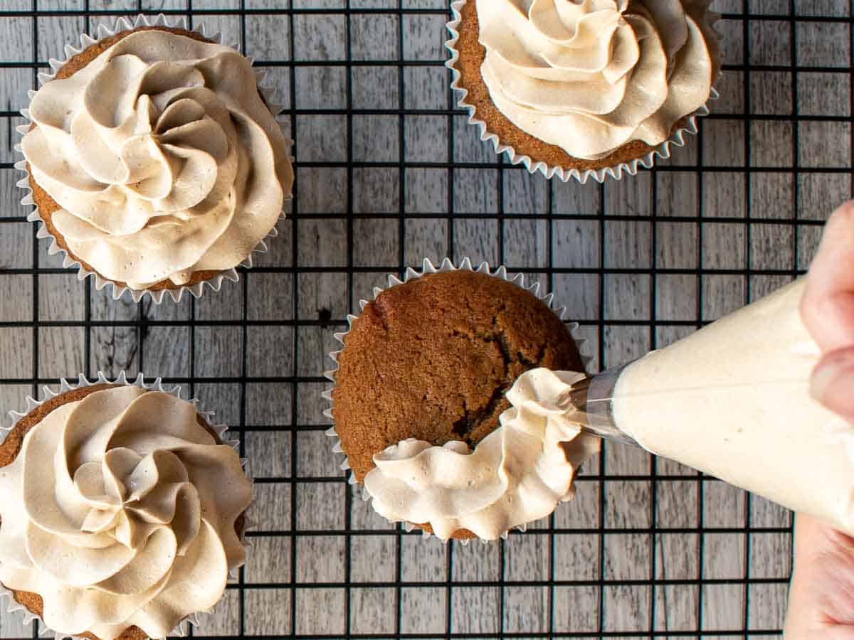 Off white buttercream being piped onto brown cupcakes.