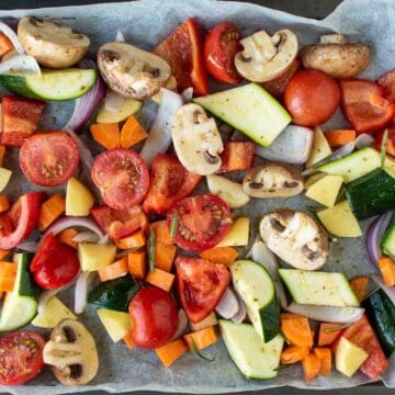 Assorted chopped vegetables in a single layer on a baking sheet viewed from above.
