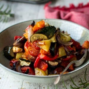 Plate of Italian Roasted Vegetables piled high with a spoon inserted and a red napkin in the background.