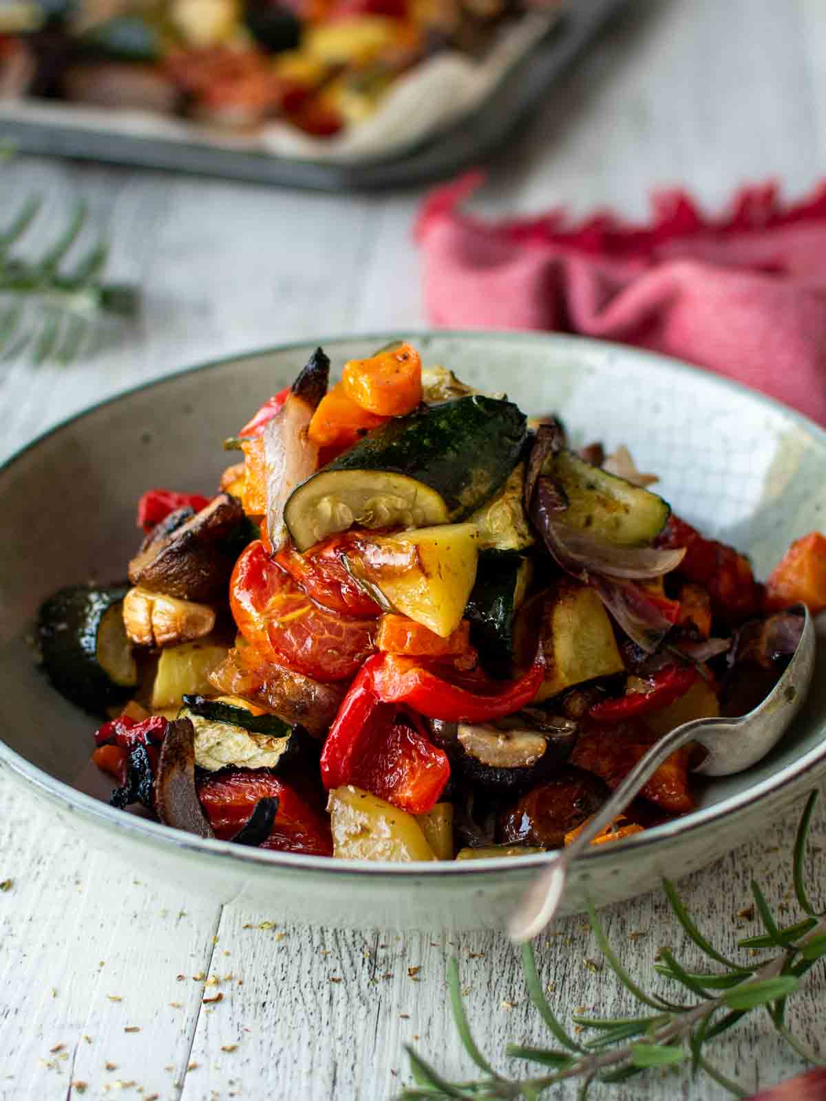 Plate of Italian Roasted Vegetables piled high with a spoon inserted and a red napkin in the background.