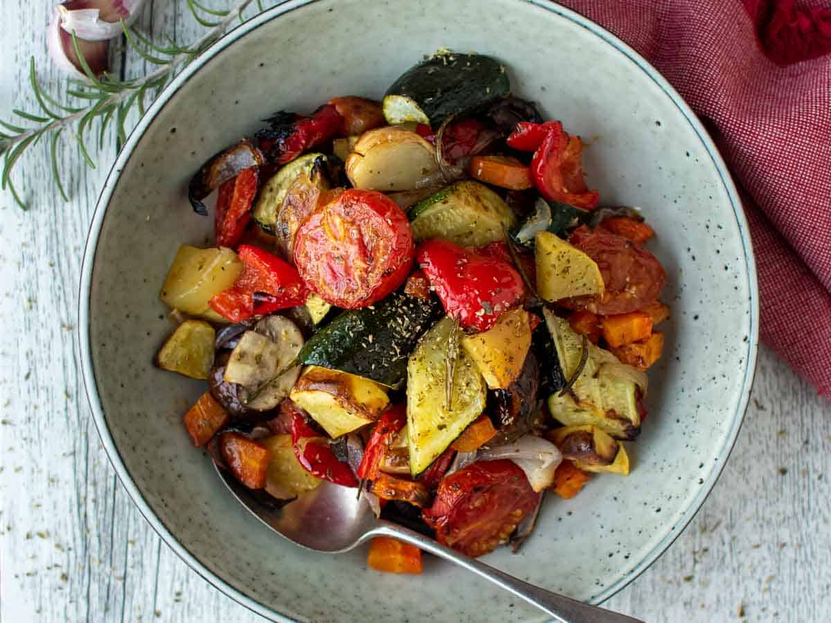 Assorted colorful chopped and roasted vegetables in a pale green bowl viewed from above.