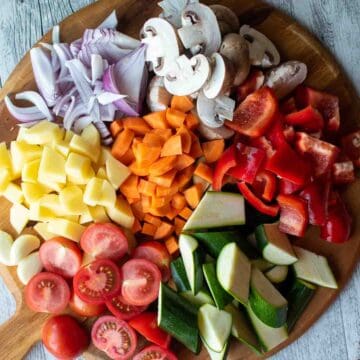 Assortment of colorful chopped vegetables on a round wooden board.