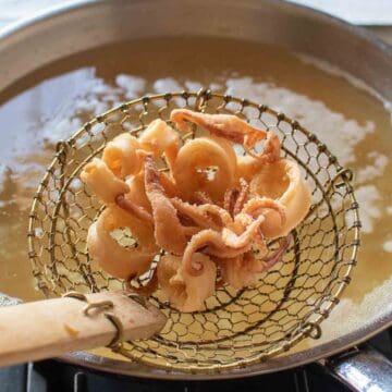 Fried calamari in a slotted spoon above an oil filled pan.