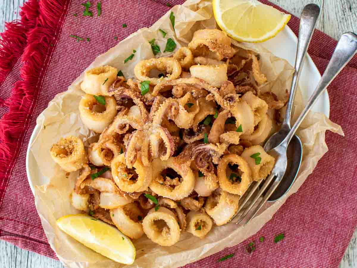 Platter of golden brown calamari rings and tentacles with lemon wedges on the side.