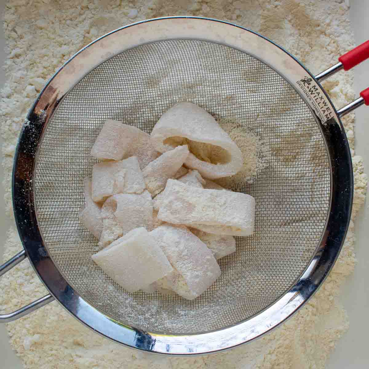 Flour coated calamari in a sieve to remove excess flour.