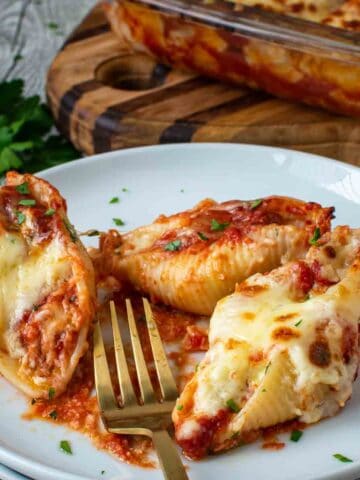 Three giant cheese stuffed shells on a stack of white plates with a gold fork.