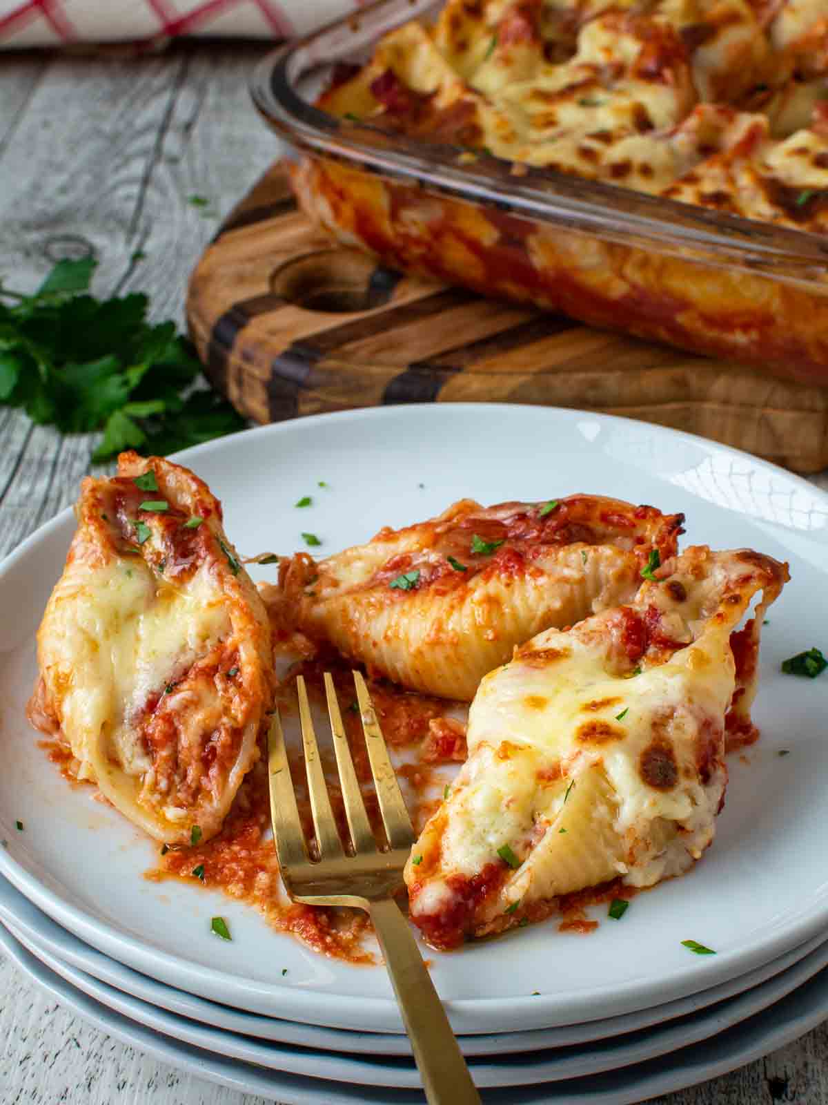 Three giant cheese stuffed shells on a stack of white plates with a gold fork.