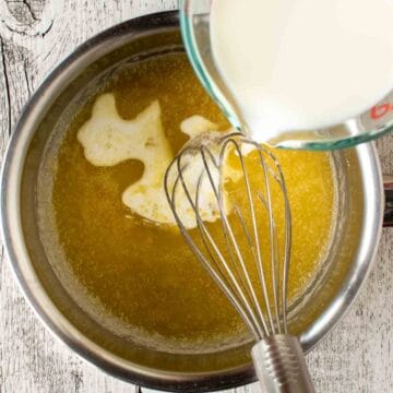 Milk being poured into a butter mixture in a stainless steel pan with a whisk in it.