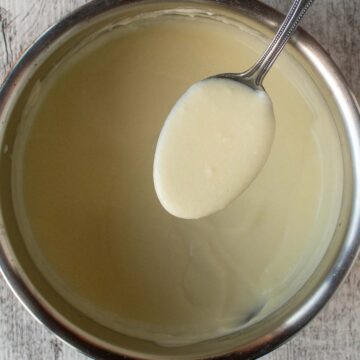 White sauce in a spoon suspended above a pan full of the white sauce.