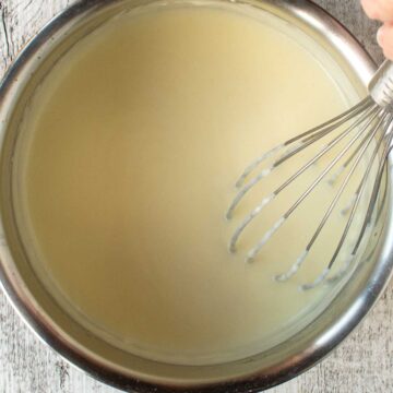 White sauce in a pan being stirred with a whisk.