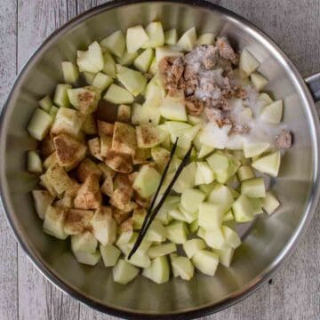 Apples, ground cinnamon, sugar and a split vanilla bean in a stainless steel pan.