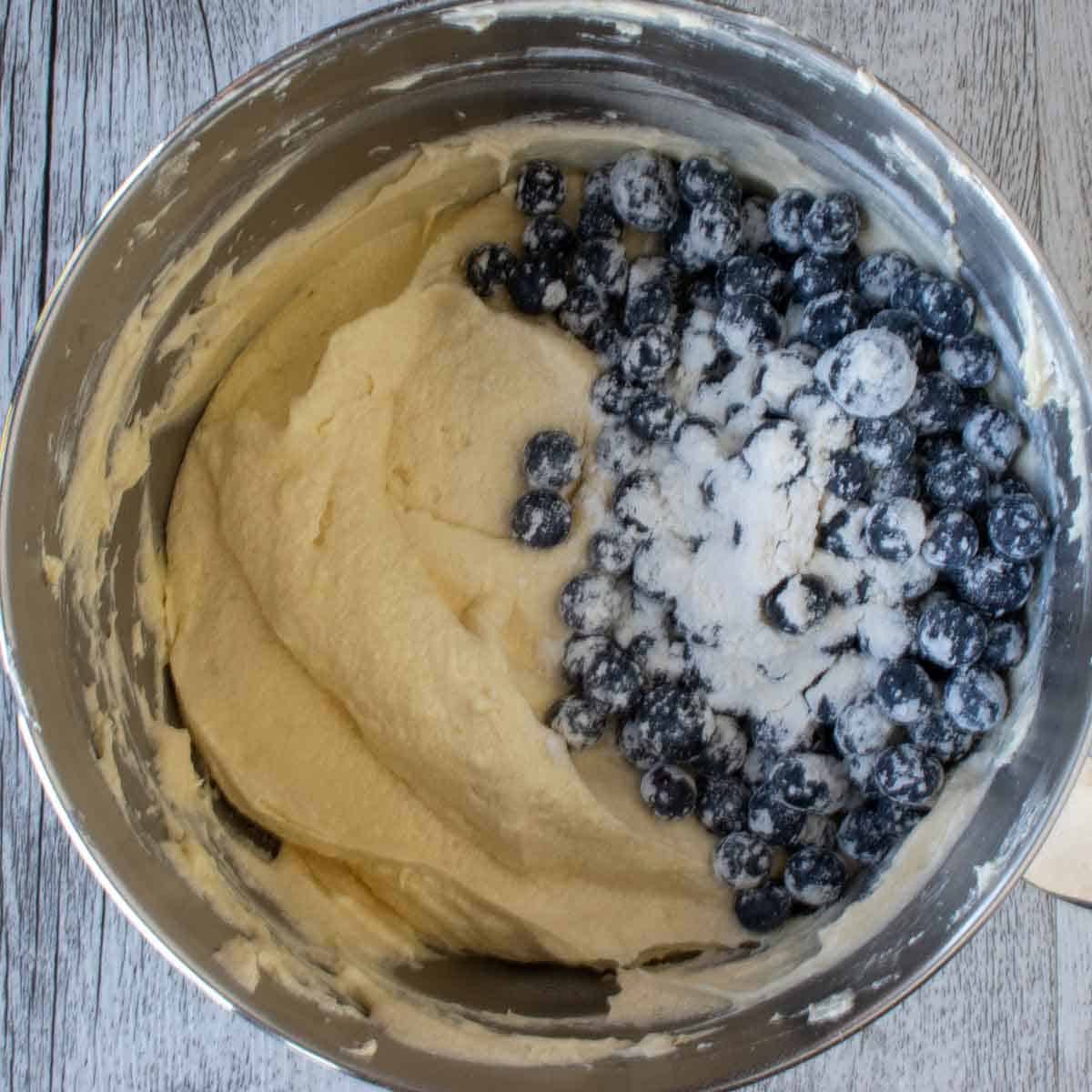 Cake batter, fresh blueberries and a sprinkle of flour in a stainless steel bowl.
