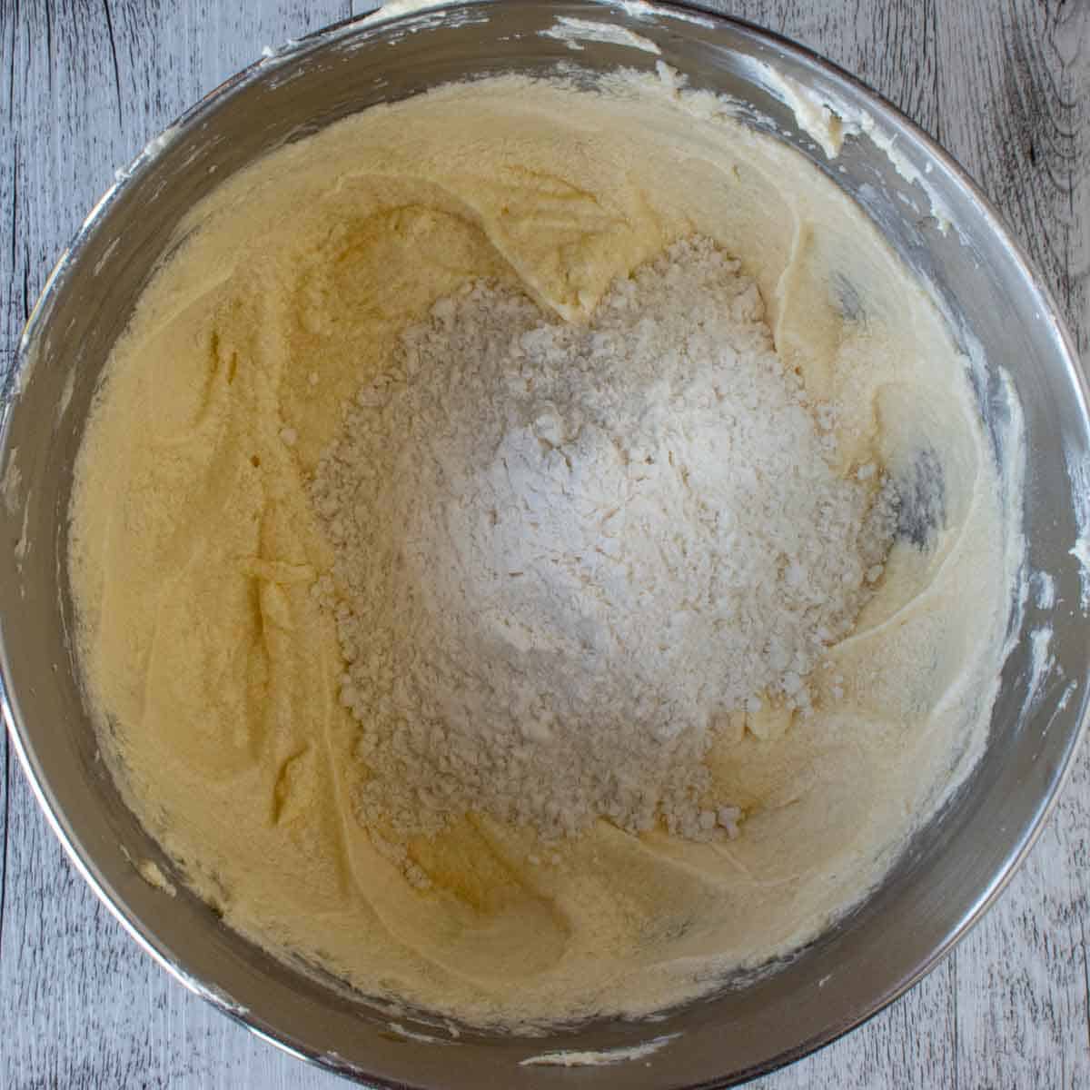 Pale yellow creamy mixture with some flour on it in a stainless steel bowl.
