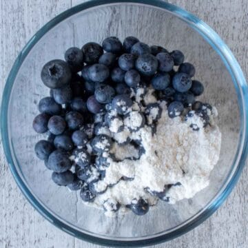 Blueberries and a spoonful of flour in a clear glass bowl.