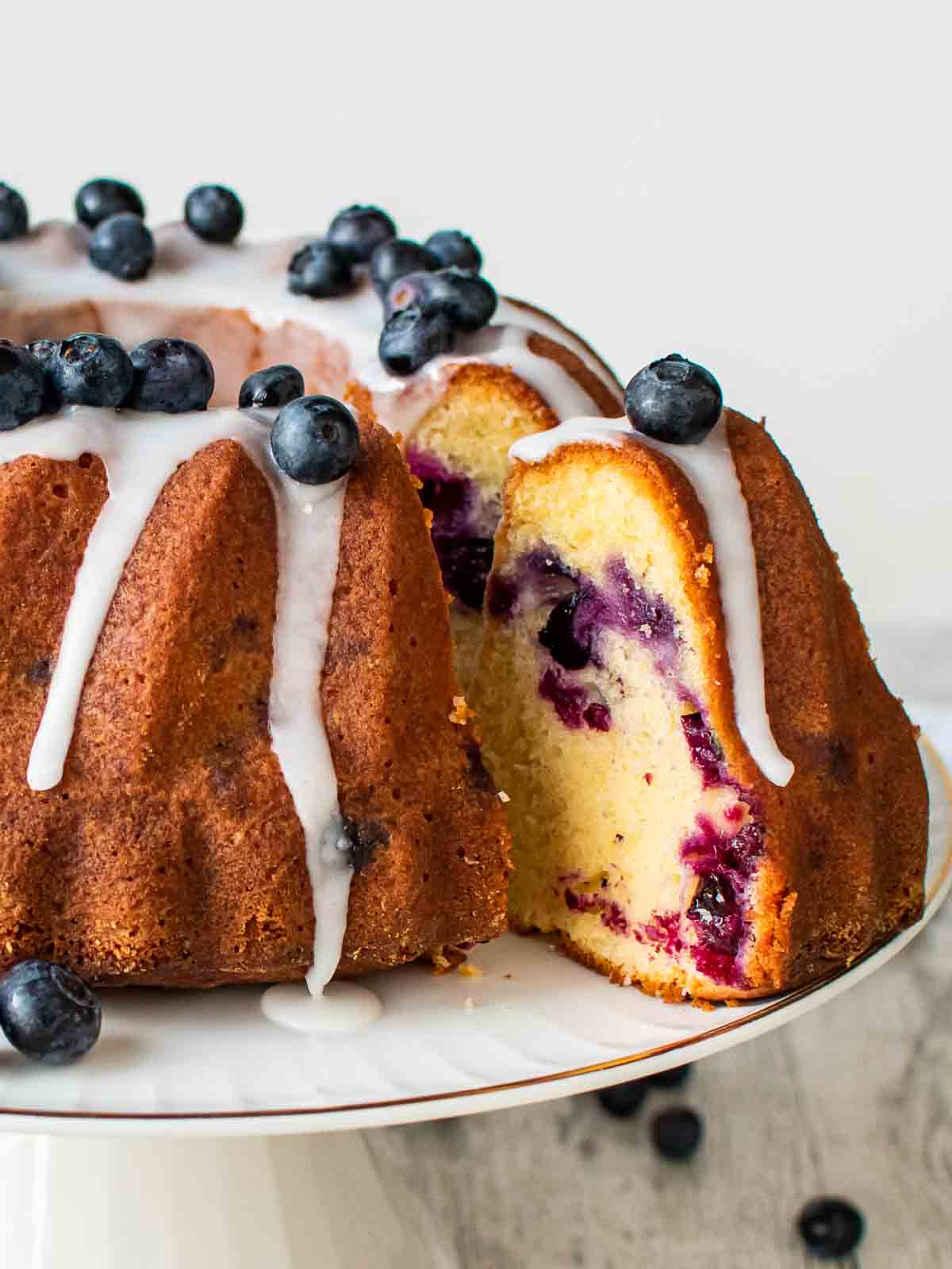 Blueberry pound cake on a white cake stand with a slice cut and pulled out.