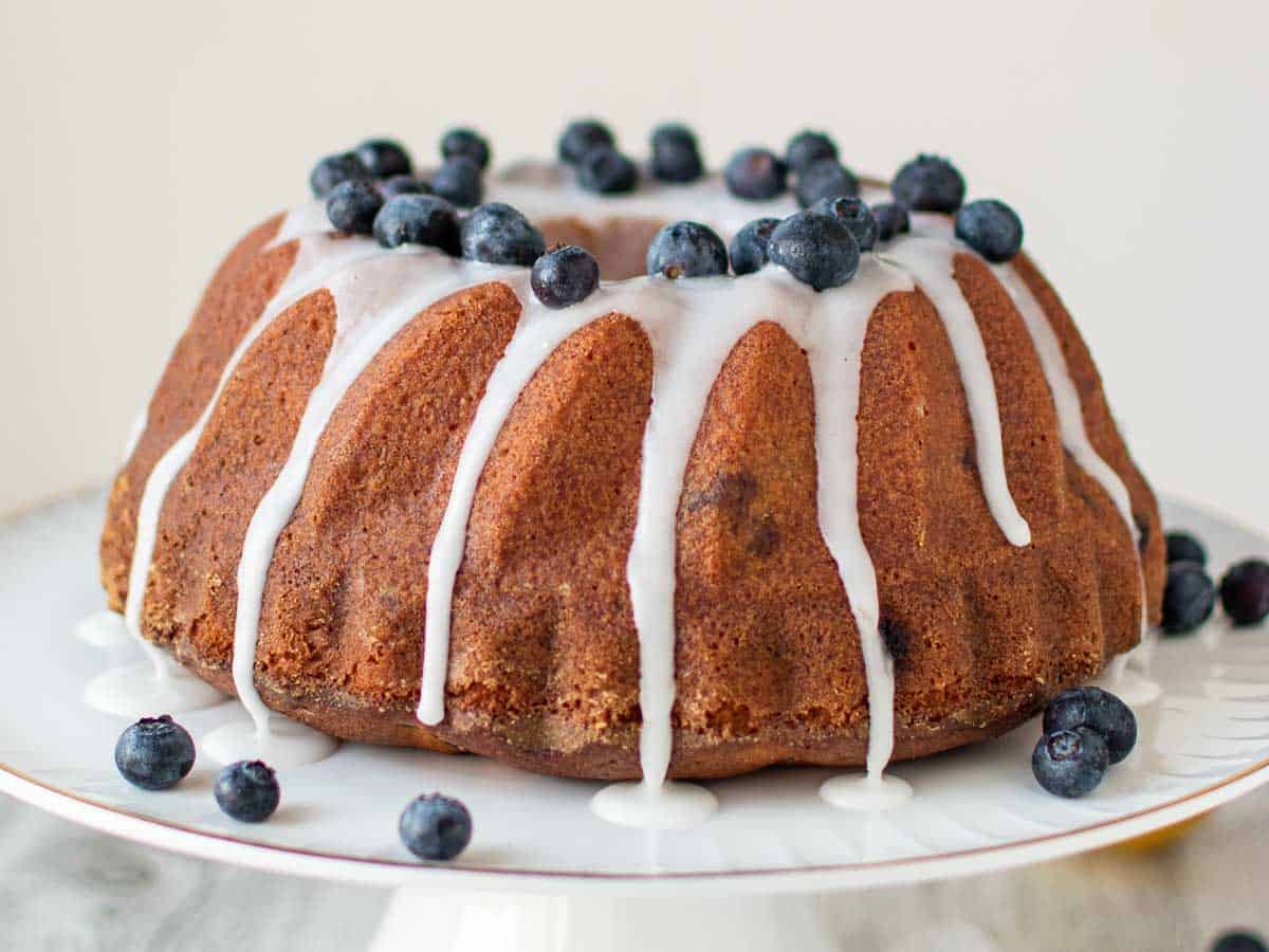 Whole bundt cake with white glaze drizzling down and blueberries on top.