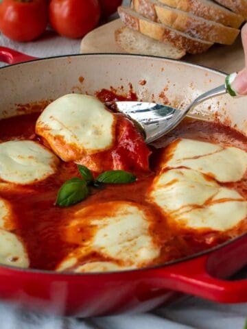 Chicken Pizzaiola in a red skillet with one piece being lifted out with a spoon.