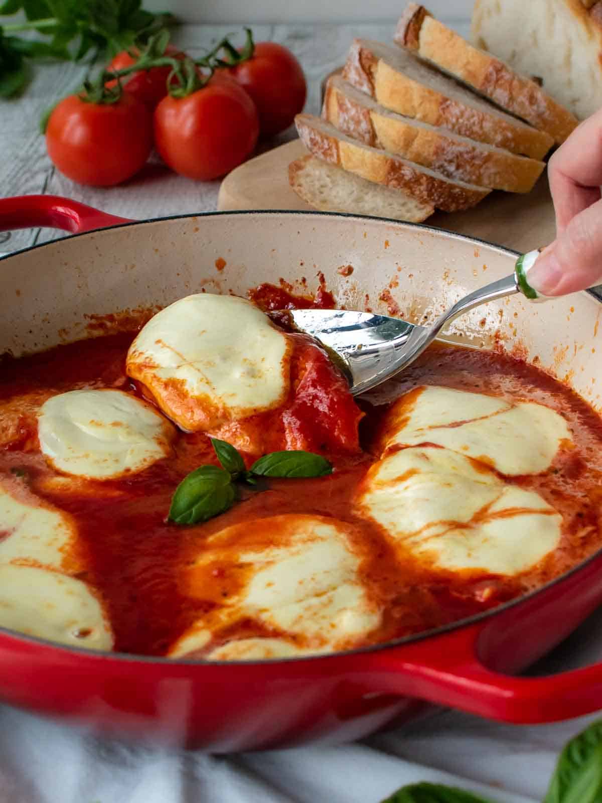 Chicken Pizzaiola in a red skillet with one piece being lifted out with a spoon.