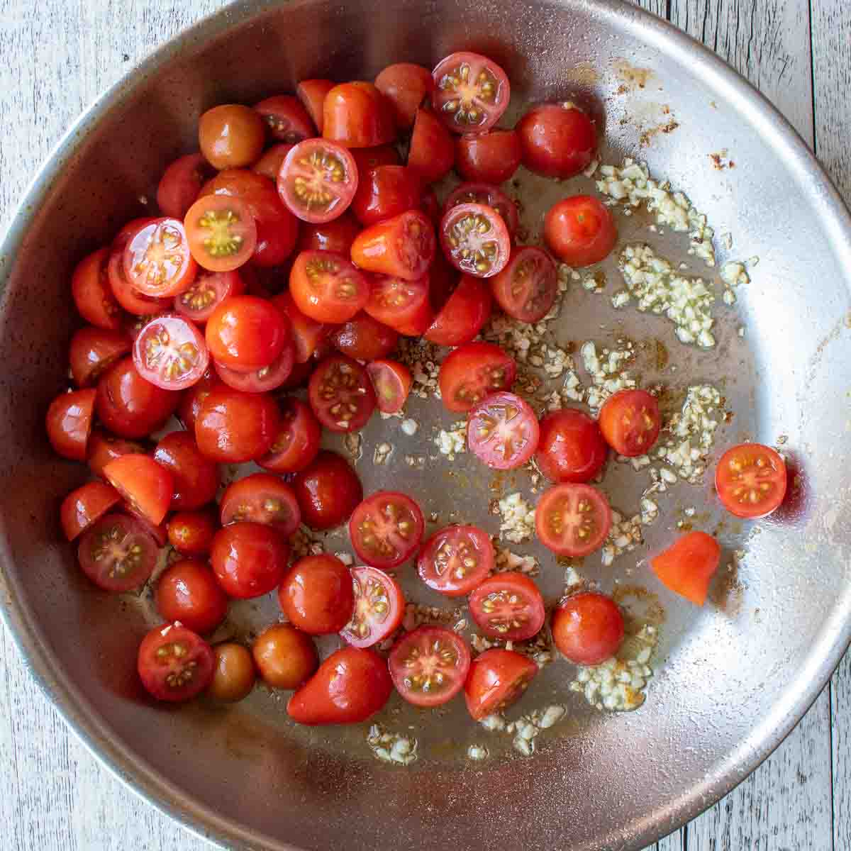 Halved cherry tomatoes and chopped garlic in a stainless steel pan.