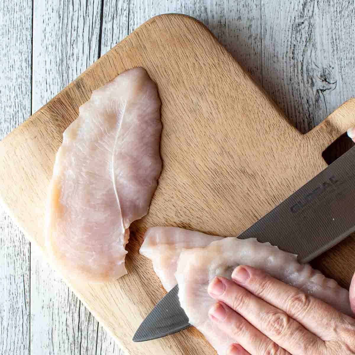 Chicken breasts being cut through the center into thinner slices.