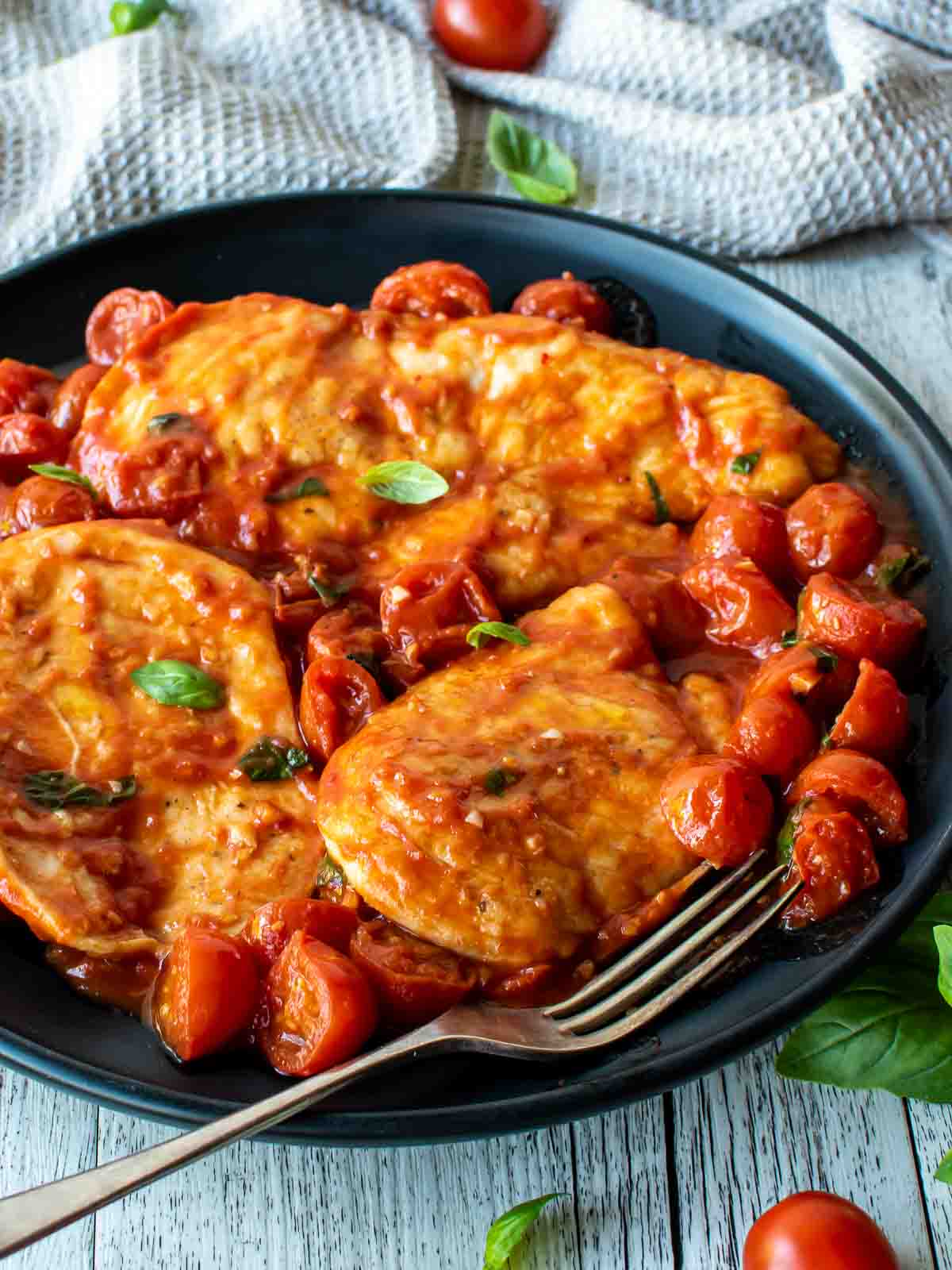 Chicken pomodoro with cherry tomatoes and fresh basil scattered around on a black plate.