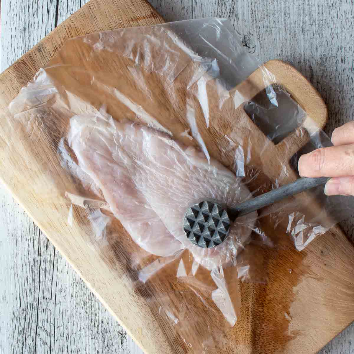 Chicken cutlet covered in plastic being pounded with a meat mallet.