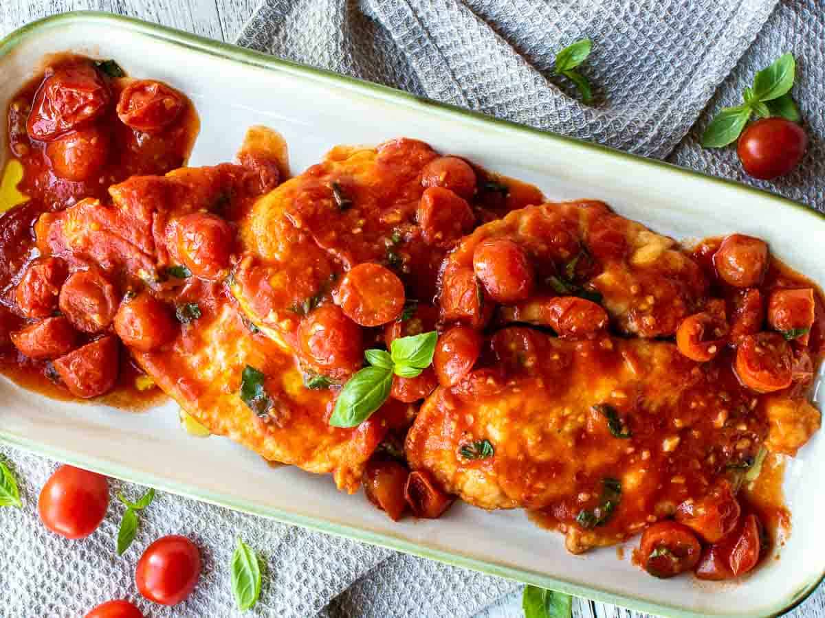 Chicken cutlets in a tomato sauce on an oblong platter.