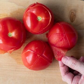 Four blanched tomatoes with skins being peeled.