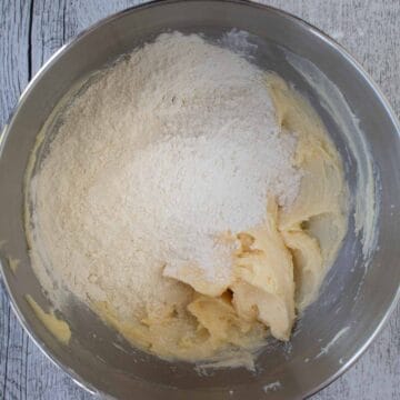 Flour on top of pale yellow creamy mixture in the bottom of a steel bowl.