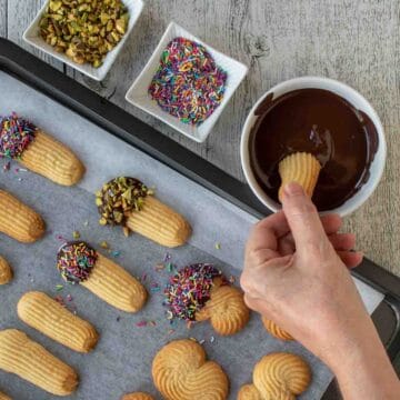 Baked cookies being dipped in chocolate and colored sprinkles.