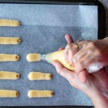 Cookie dough being piped out of a open star tip in finger long lengths.